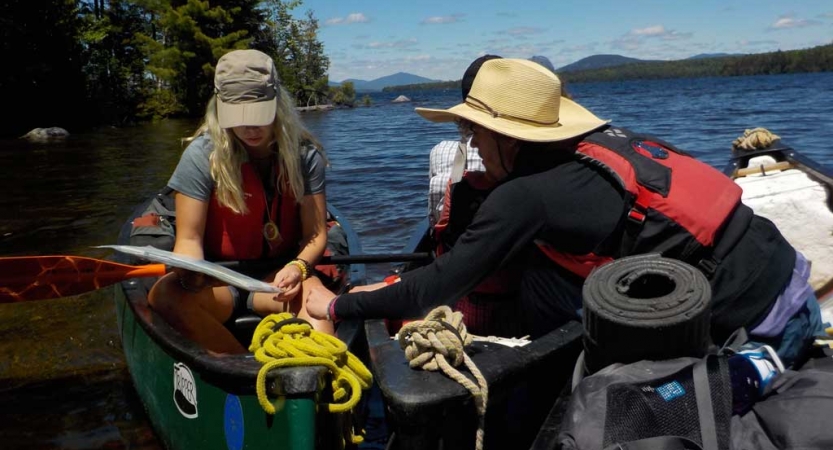 People wearing life jackets sit in canoes and examine a map